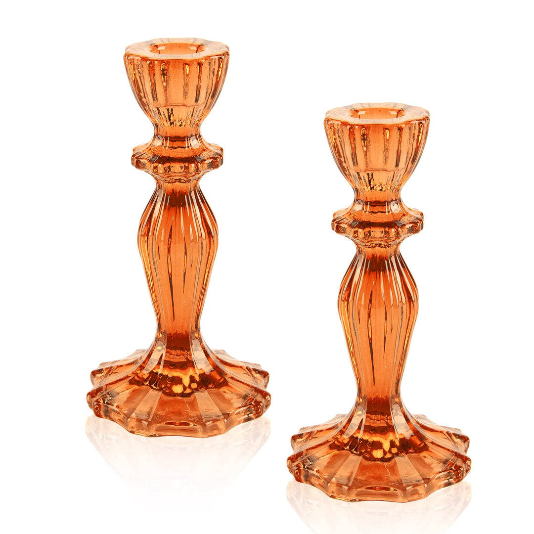 Zwei orangefarbene Stumpenkerzenhalter aus Glas auf einem dekorierten Tisch